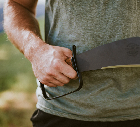 A close-up of a backcountry camper holding a Woodman’s Pal land clearing tool in his hand.