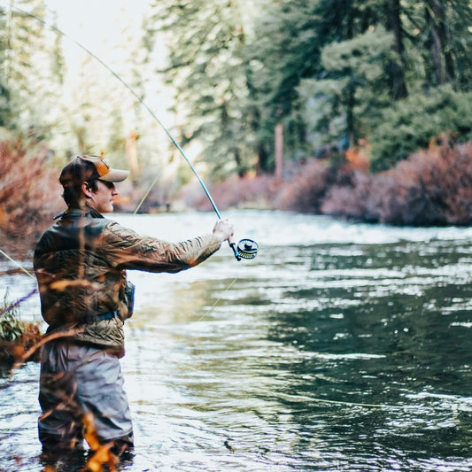 A fisherman wading in a river casting his fly fishing line into the water.
