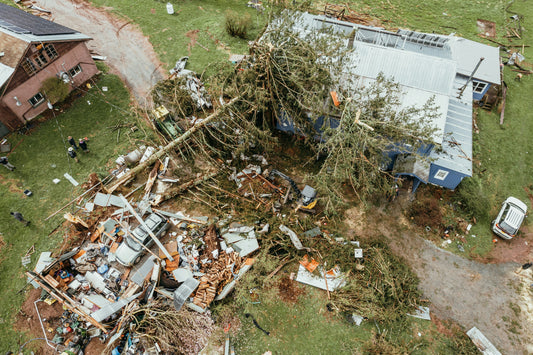An aerial view of a house damaged by a storm with a downed tree and various other pieces of debris surrounding the property.