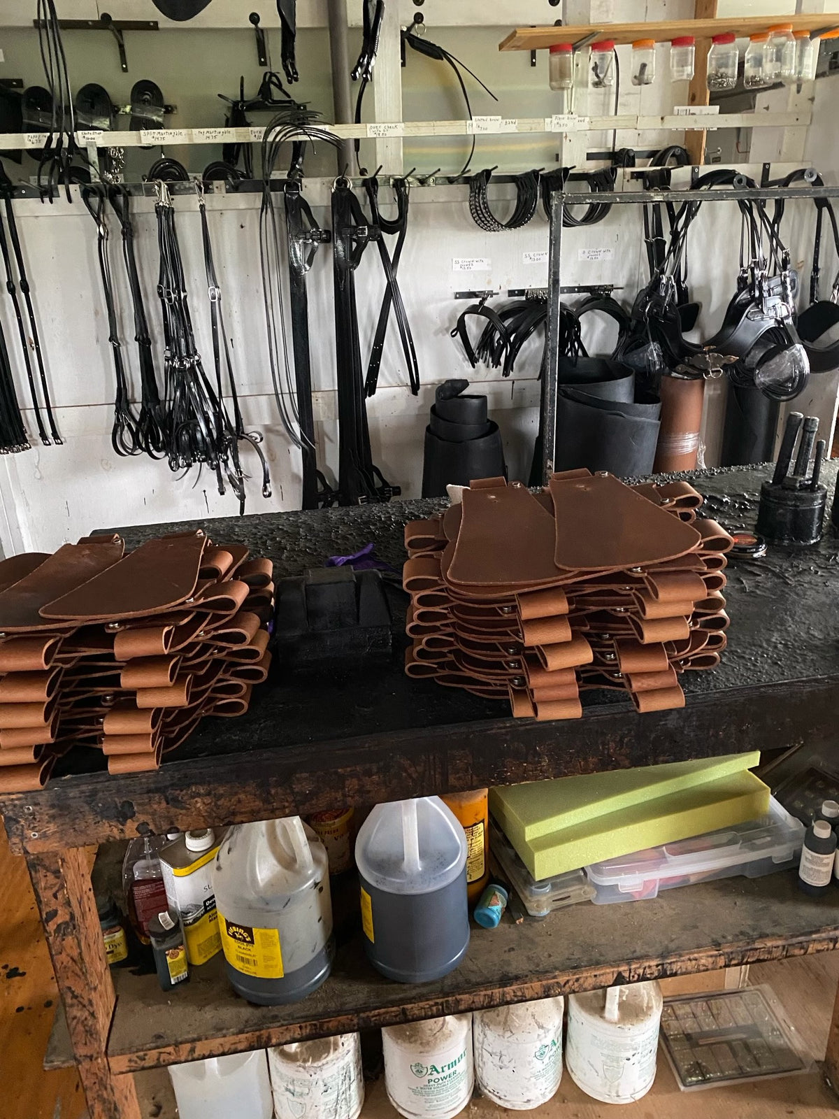 Two stacks of finished leather machete sheaths with belt loops on a workbench