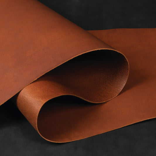 Roll of smooth, golden-brown Buffalo leather curled on a dark background, showcasing its texture and natural grain. 