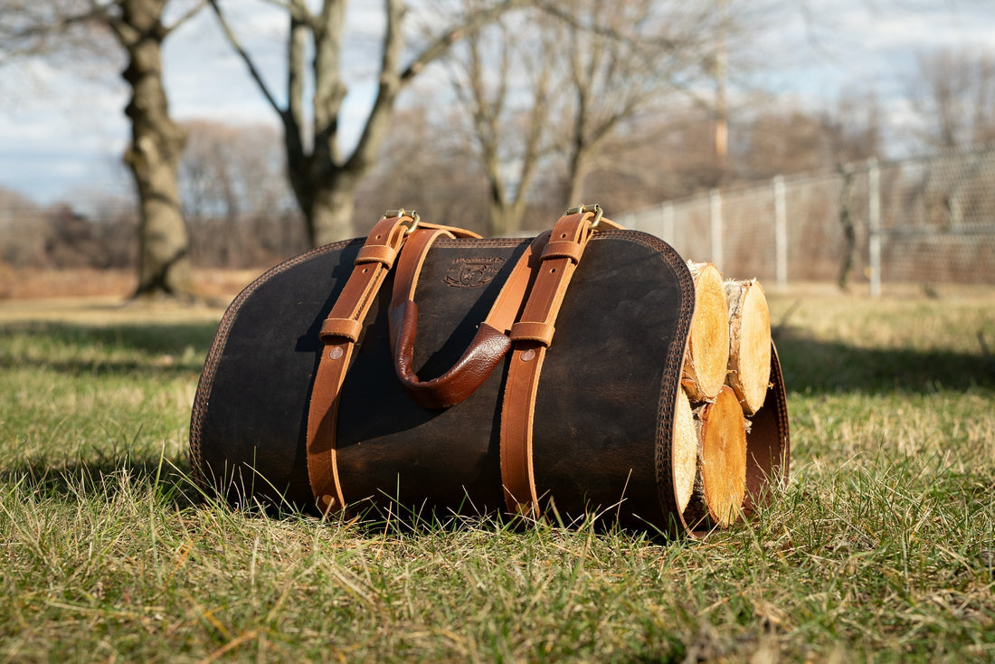 A Woodman’s Pal leather log carrier holding cut firewood, resting on grass outdoors, with sturdy straps and handles designed for carrying firewood to a fireplace or campfire