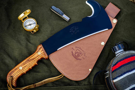 The original Woodman’s Pal survival machete with leather sheath, surrounded by outdoor gear. 