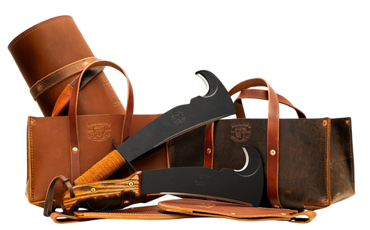 Woodman’s Pal leather log carrier and tool totes displayed with two machetes featuring wood and leather handles, and leather sheathes. 