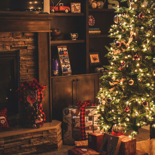 A christmas tree in a room with a fireplace and shelves with gift-wrapped presents underneath the tree. 