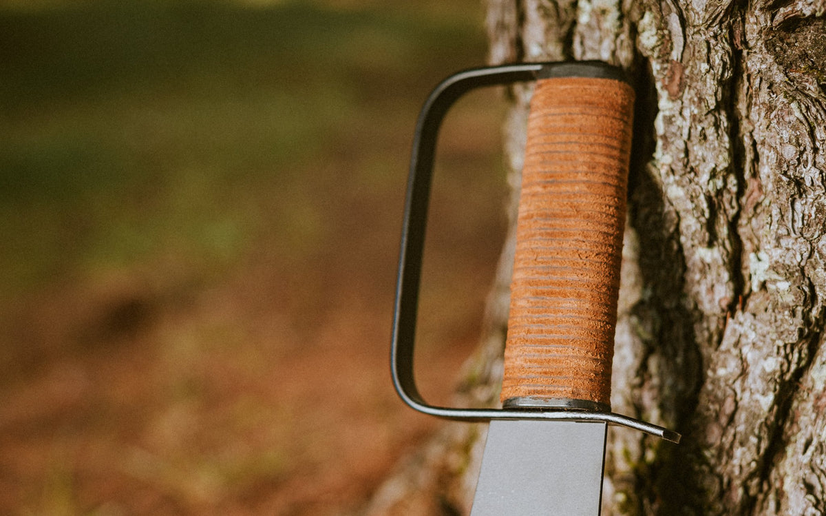 Stacked leather handle and steel knuckle guard of the Woodman's Pal against tree bark