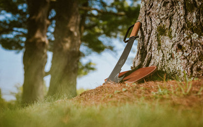 Leather-handle Woodman's Pal machete and sheath leaning against a tree