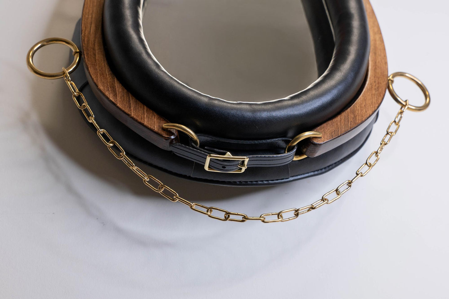 Close-up of brass chain, buckle, and lower leather padding on equestrian mirror